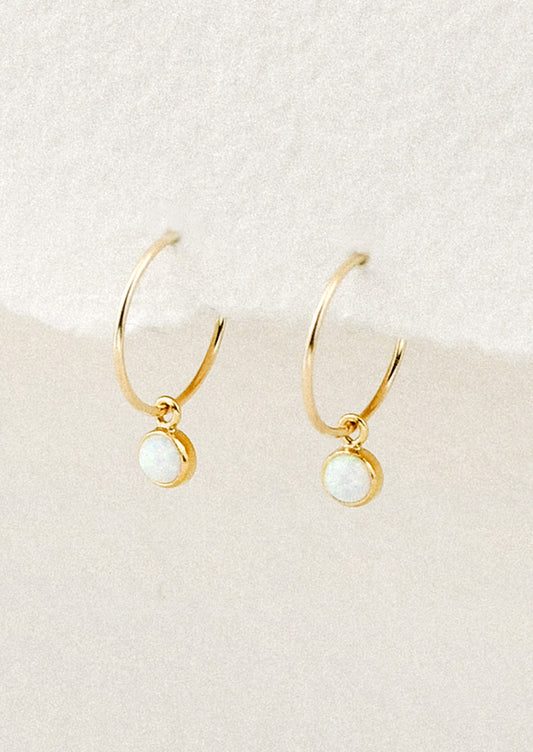 A pair of small gold hoop earrings with bezeled opal charms.