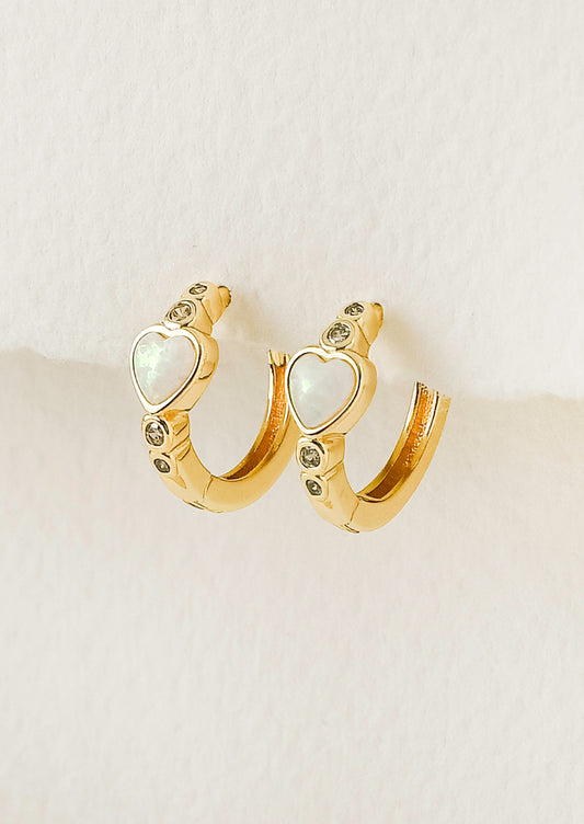 A pair of gold hoop earrings with a heart=shaped opal in the center and tiny gems above and below.