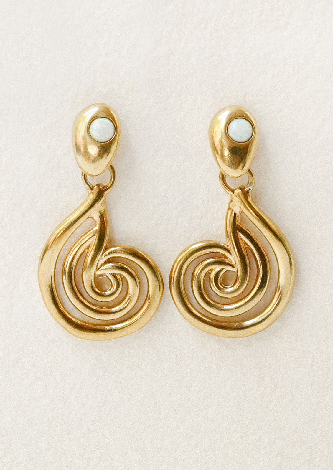 A pair of bronze earrings with a spiral design and opals at the top.
