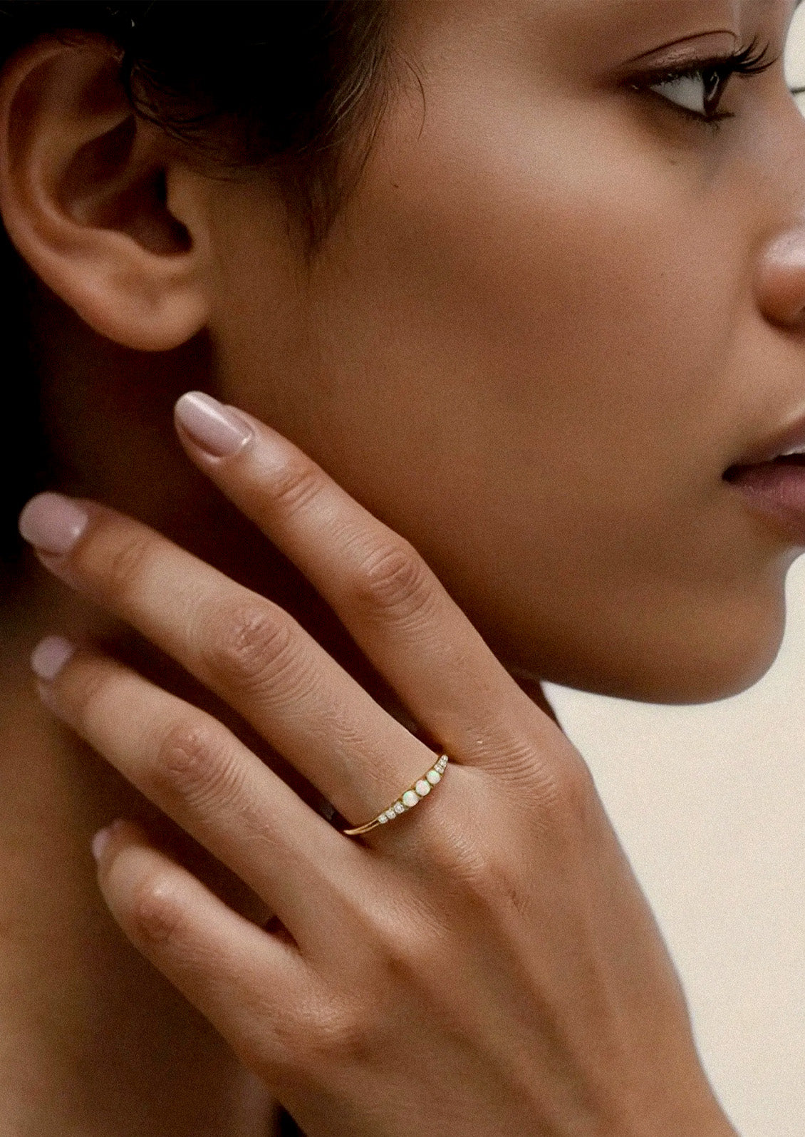 A woman wearing a gold ring adorned with three opals and cubic zirconia gems on either side.