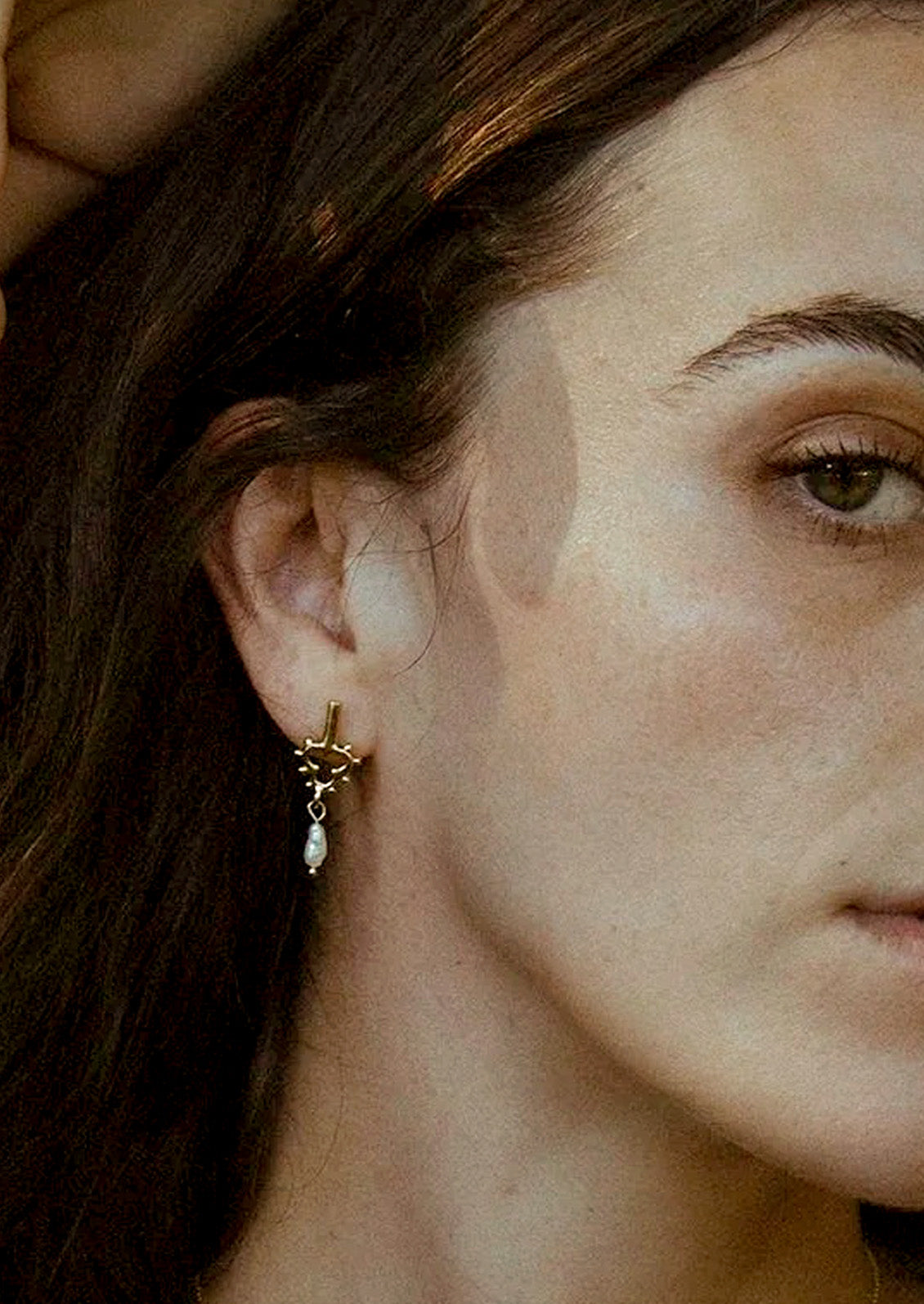 A woman wearing a unique brass earring with a dangling keshi pearl.