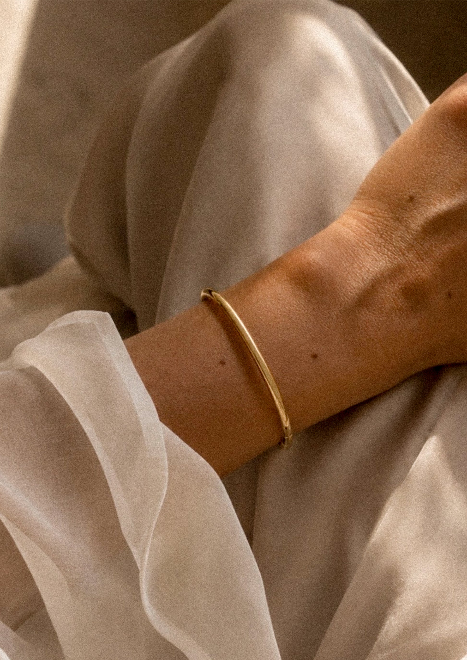 A woman wearing a minimal gold bangle bracelet on her wrist.