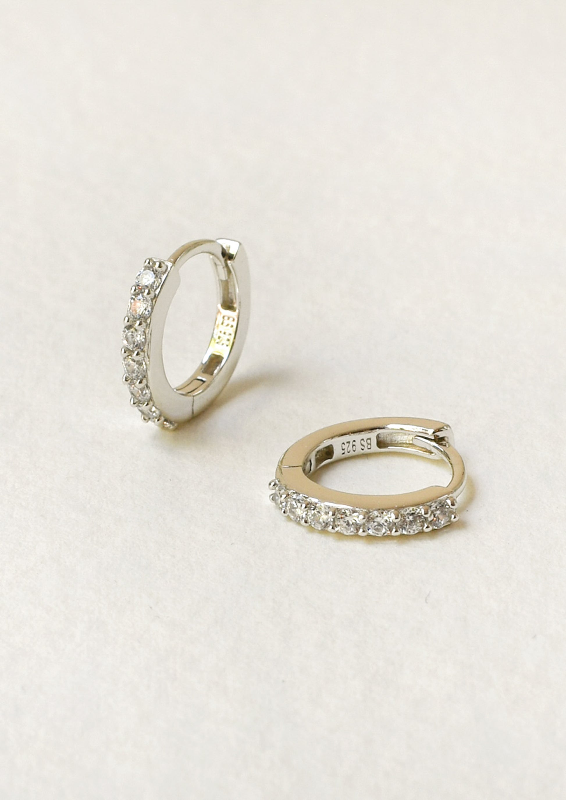 A pair of small huggie hoop earrings with clear pavé-set stones.