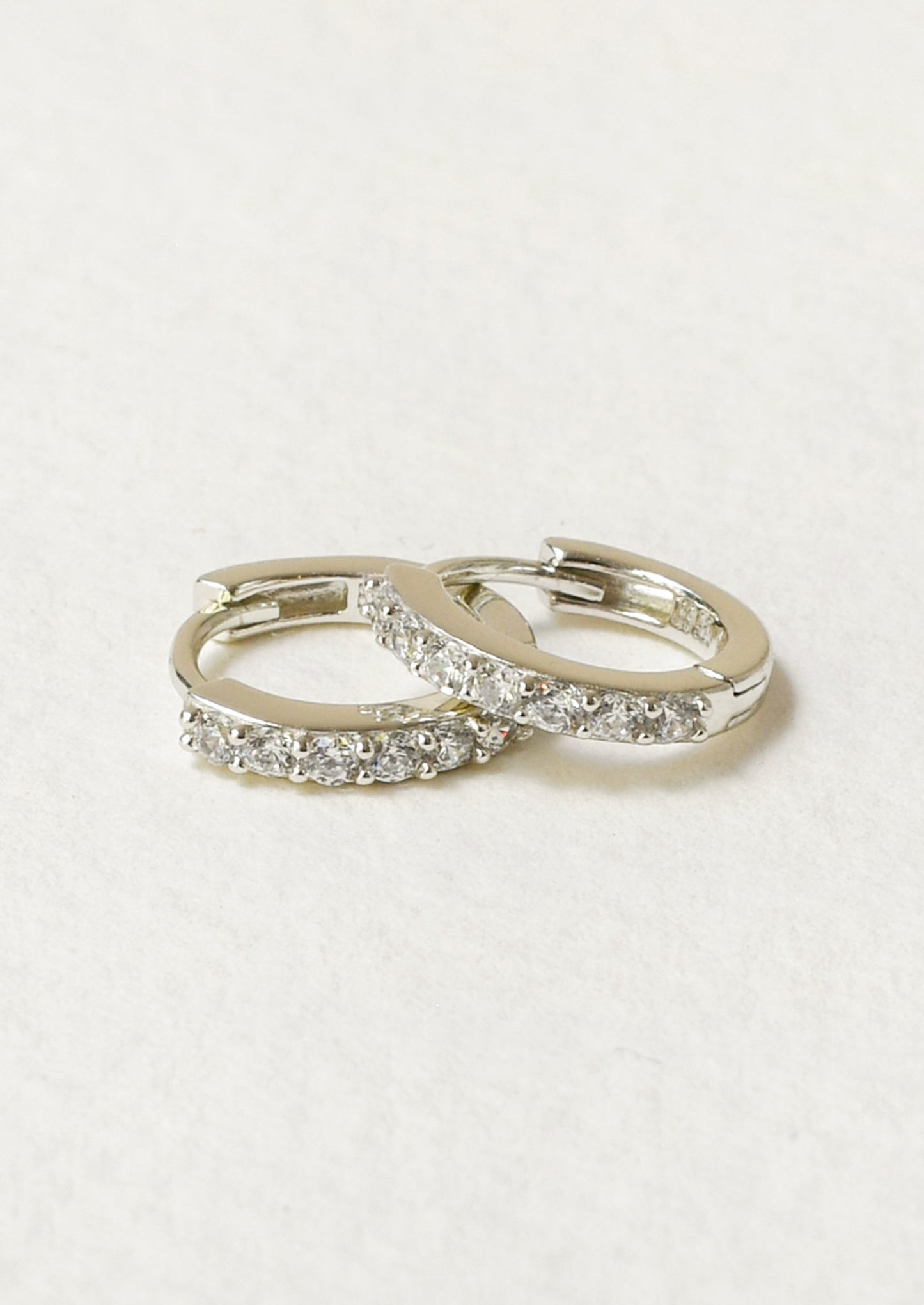 A pair of small huggie hoop earrings with clear pavé-set stones.