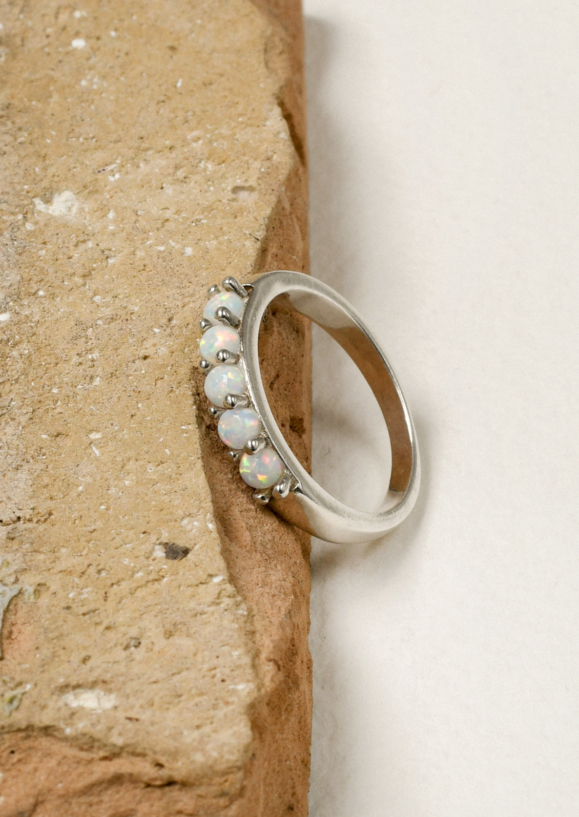A sterling silver ring adorned with 5 opals, leaning on the edge of a brown stone.