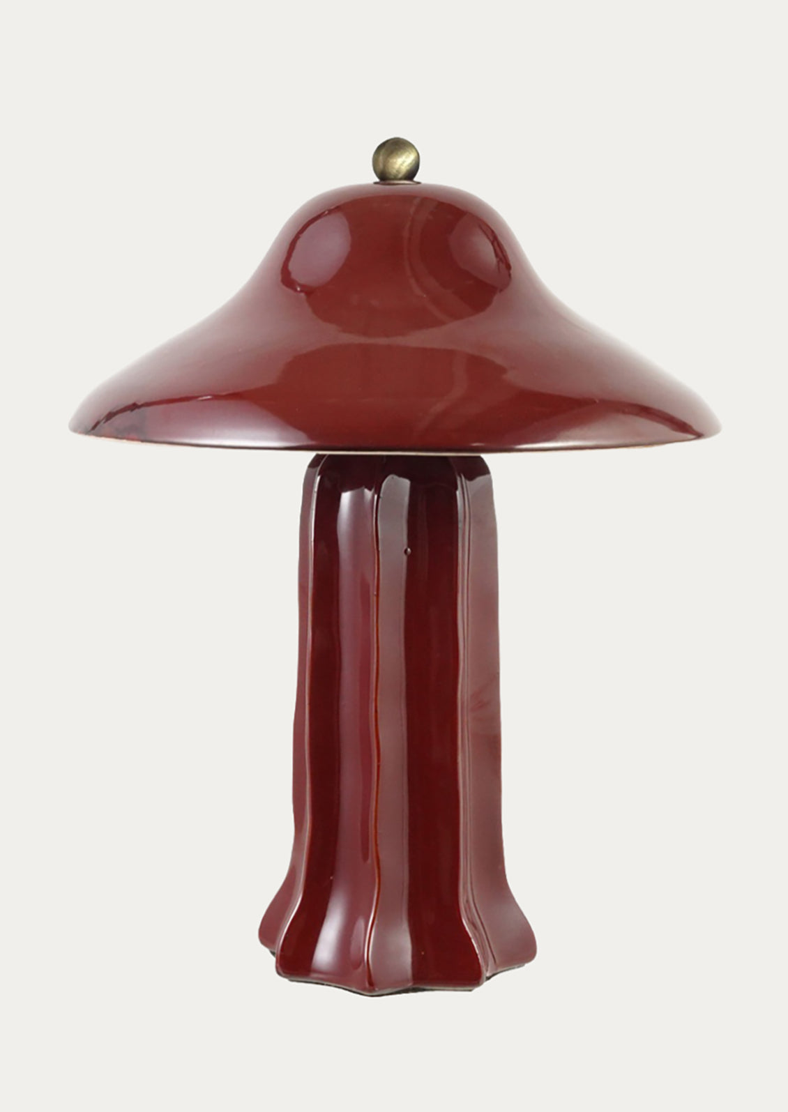 A glossy mushroom-shaped table lamp in deep burgundy with a small brass finial on top, set against a solid off-white background.
