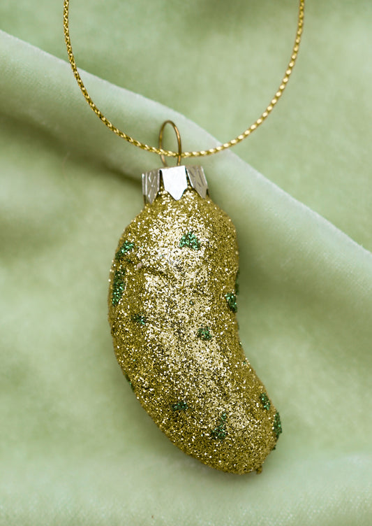 A small glass ornament of a pickle covered in green glitter.