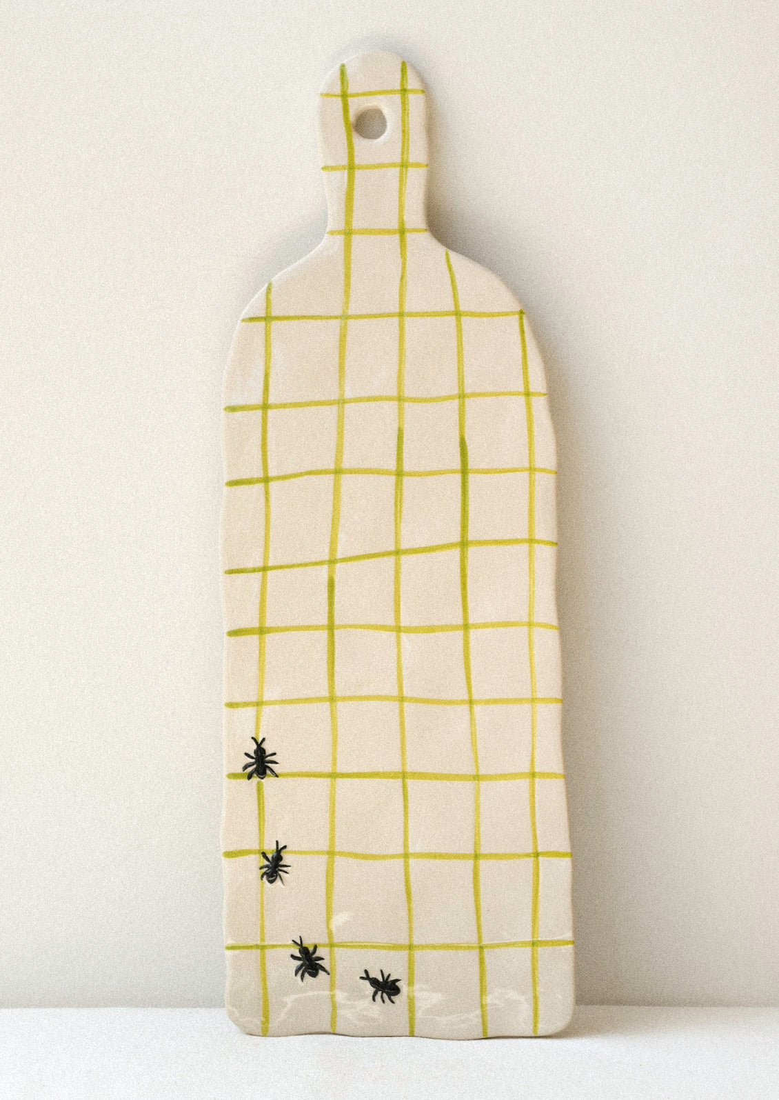 A large ceramic serving platter with green grid stripes and illustrated black ants in the corner.