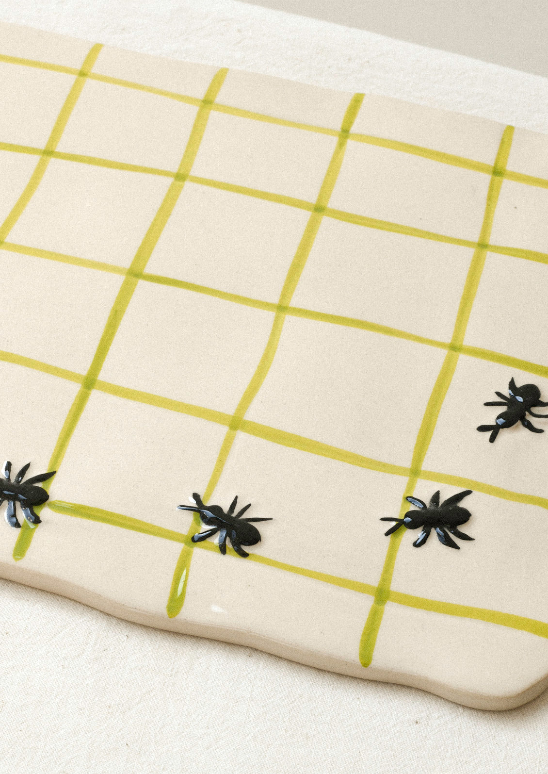 A large ceramic serving platter with green grid stripes and illustrated black ants in the corner.