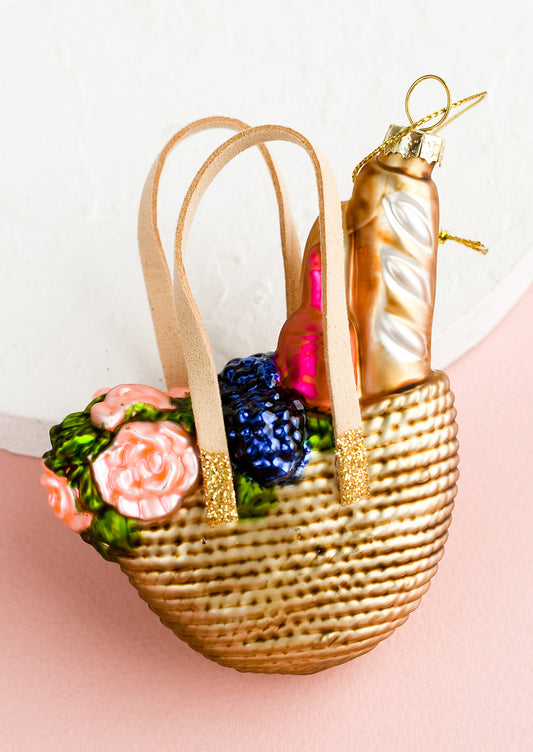 A glass ornament of a straw tote with picnic supplies.