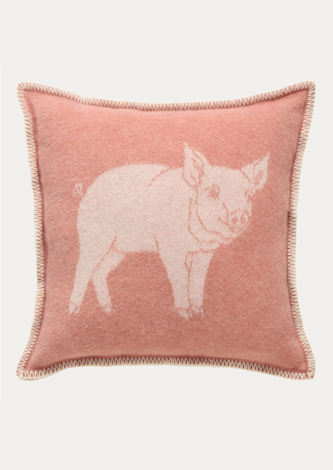 A square pink throw pillow with a light pink knitted pig design in the center and a fringed edge, shown against a plain light gray background.