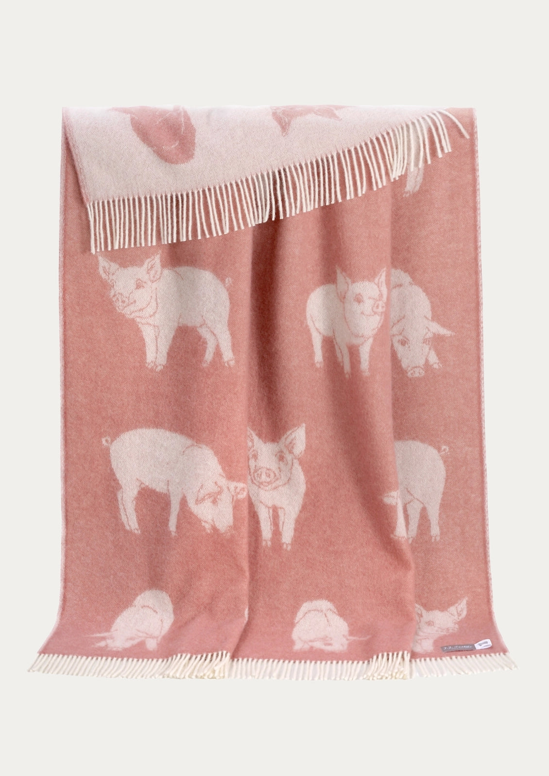 A dusty pink woven throw blanket featuring a white pattern of pigs and cream-colored fringe, displayed against a light off-white background.