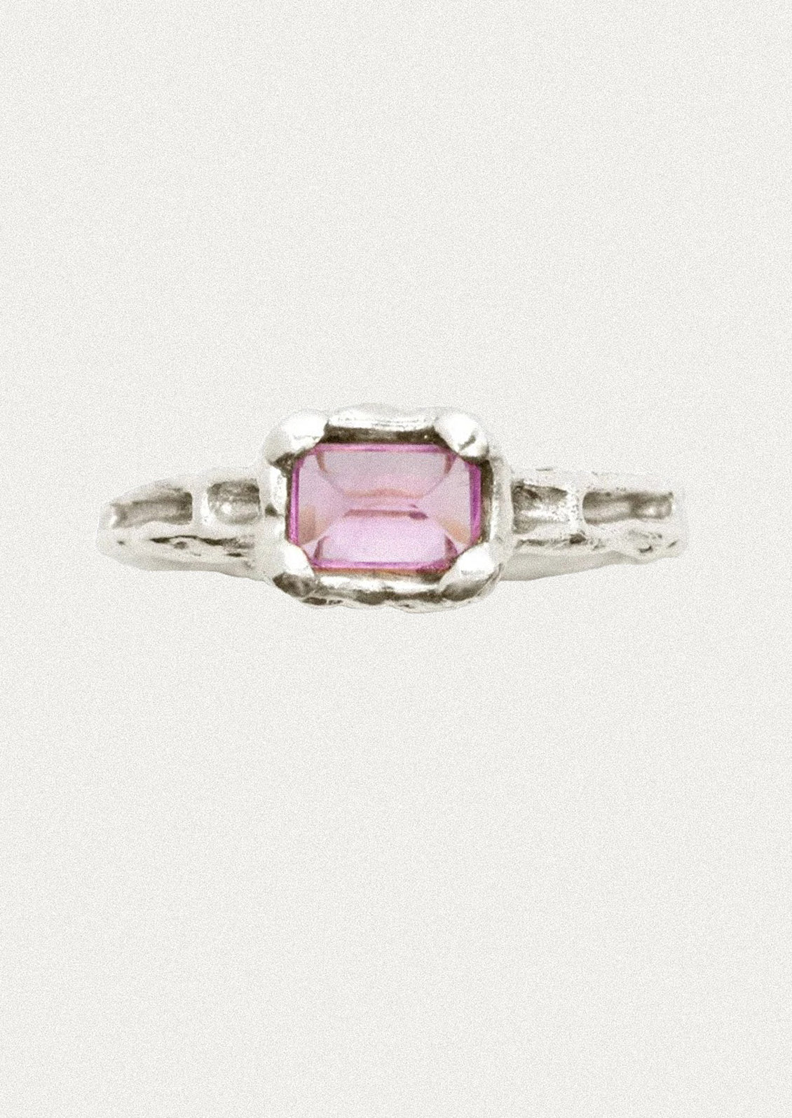 A silver ring featuring a rectangular pink gemstone in a textured bezel setting, shown against a plain off-white background.