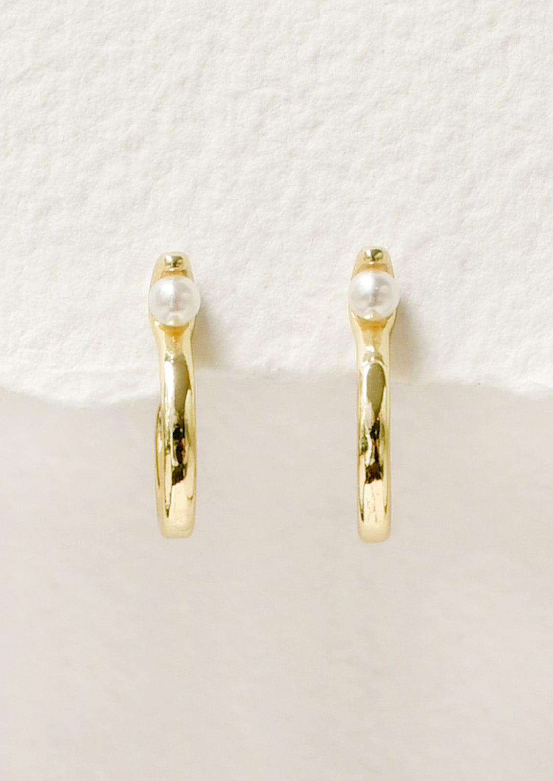 A pair of gold earrings with an "S" shaped design and a single faux pearl at the top.