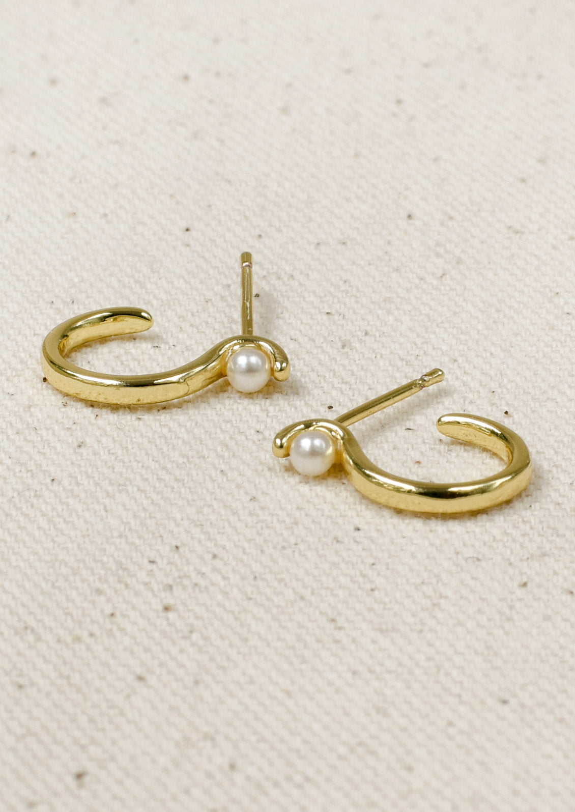 A pair of gold earrings with an "S" shaped design and a single faux pearl at the top.