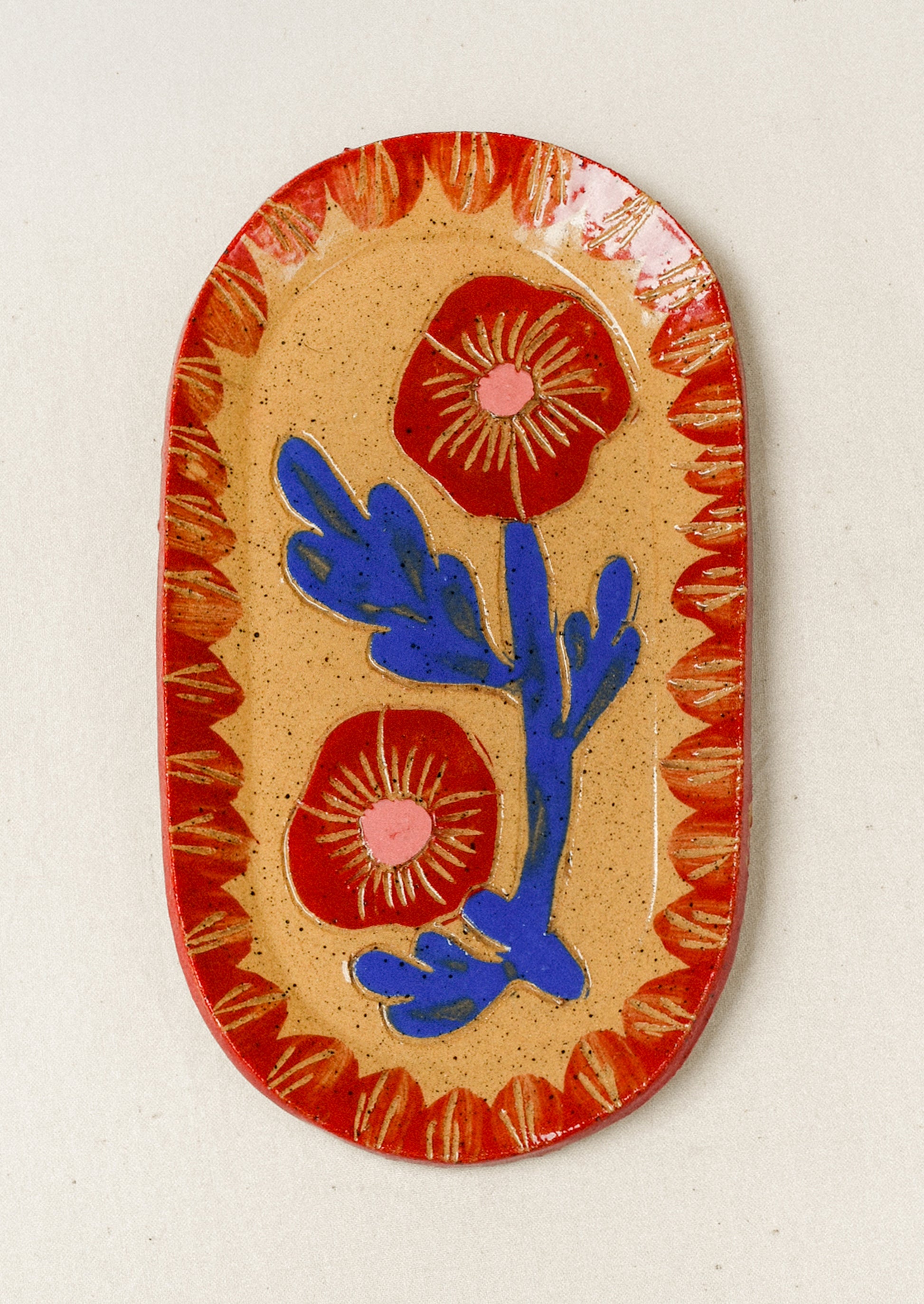 A ceramic oval catchall tray with an etched red poppy flower in the center and a red painted border.