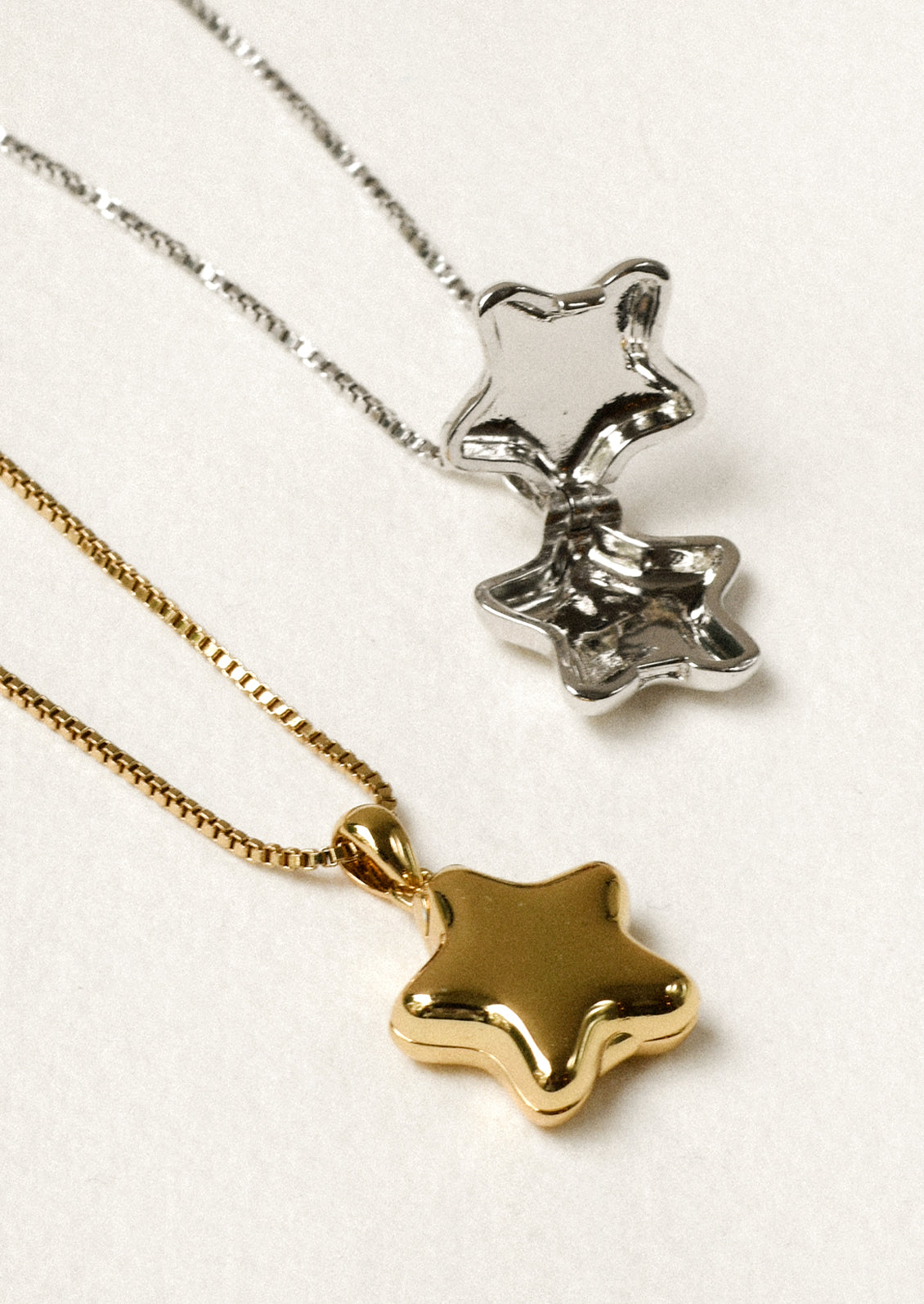 One gold and one silver necklace with a puffy star locket pendant.