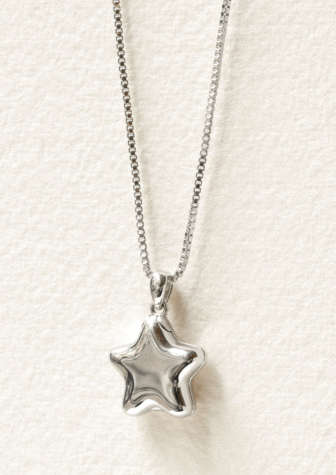 A sterling silver necklace with a puffy star locket pendant.