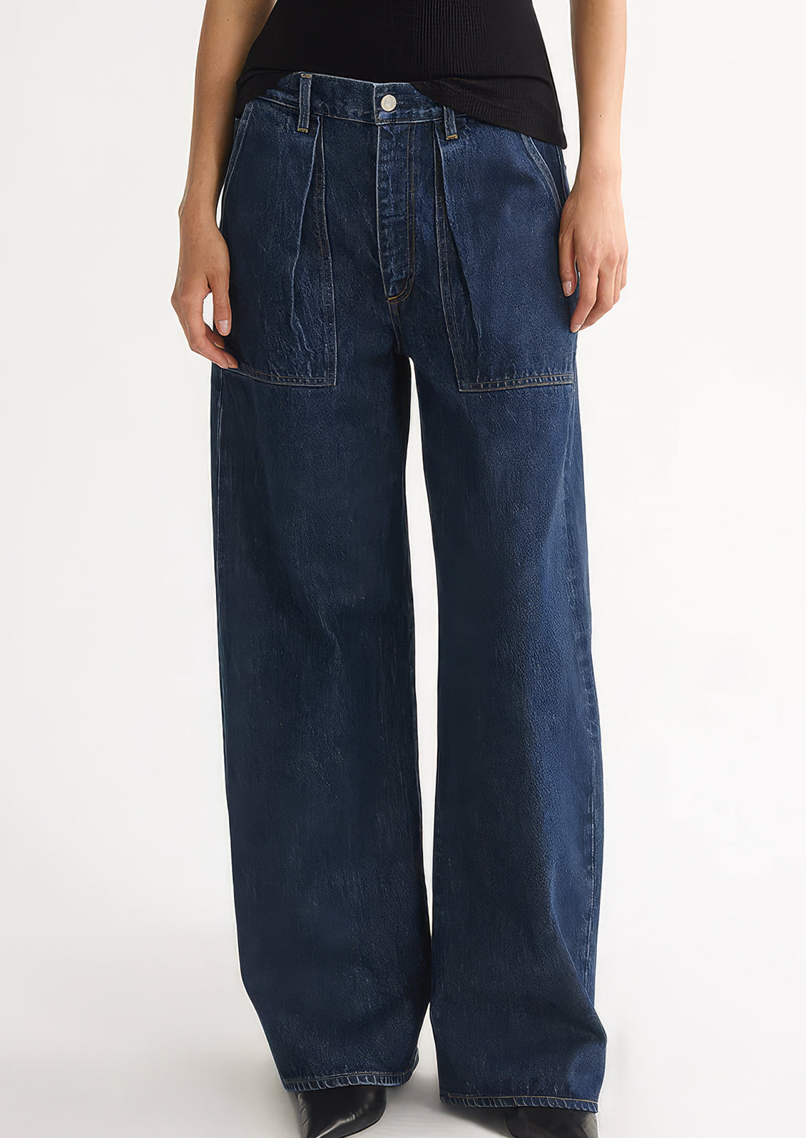 A person wearing a pair of dark denim jeans with pleated pocket front.