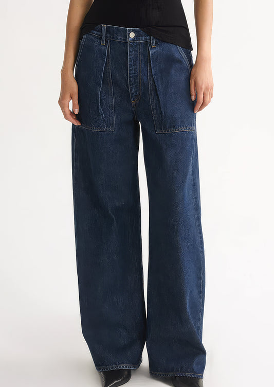 A person wearing a pair of dark denim jeans with pleated pocket front.