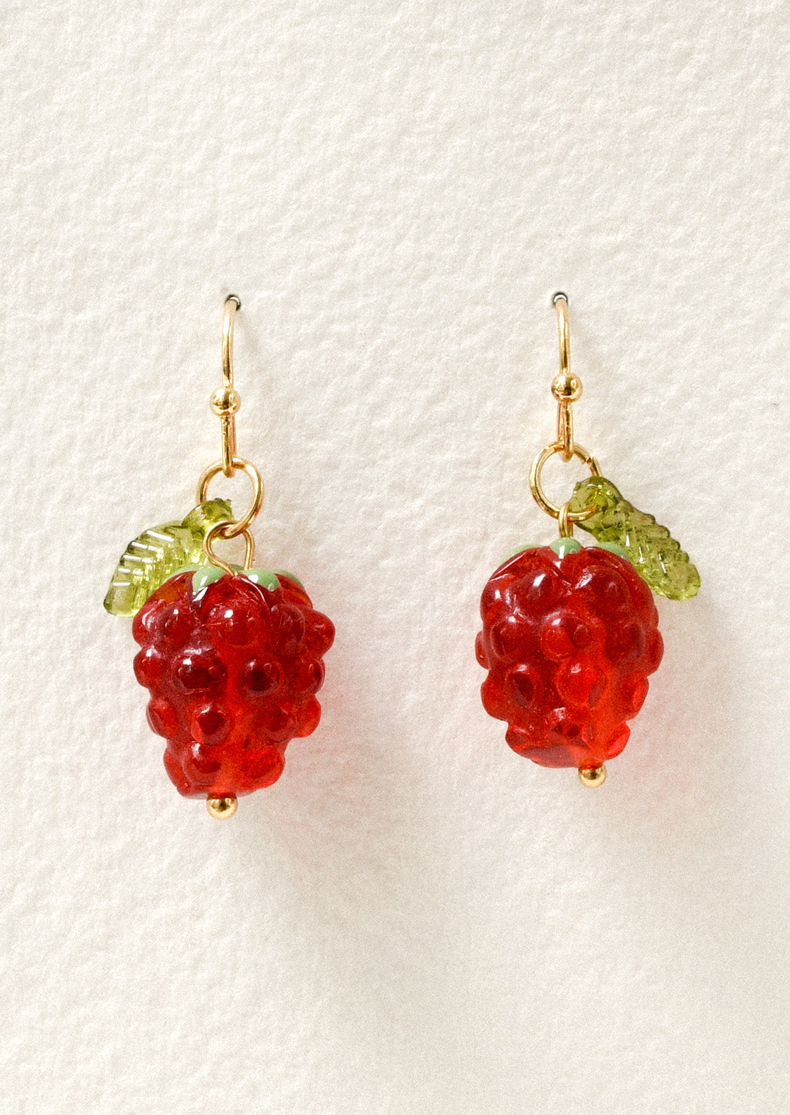 A pair of gold dangling earrings with dangling raspberry charms.