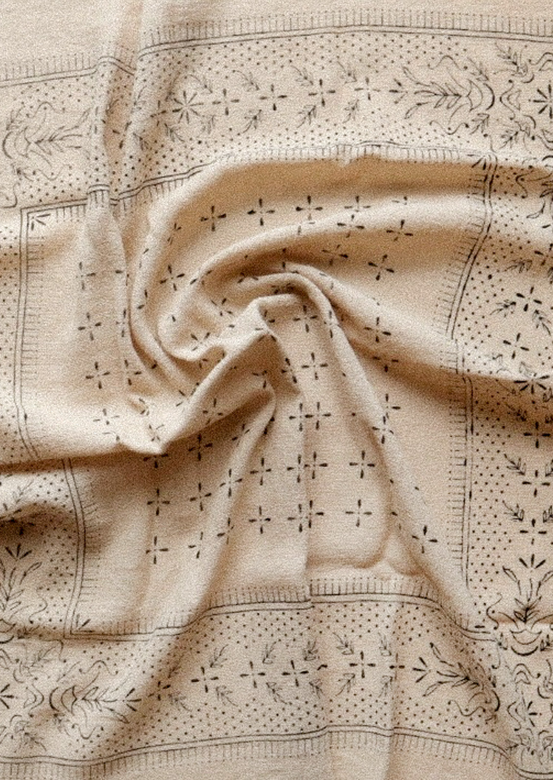 An oatmeal colored patterned scarf that is bunched up in the center.