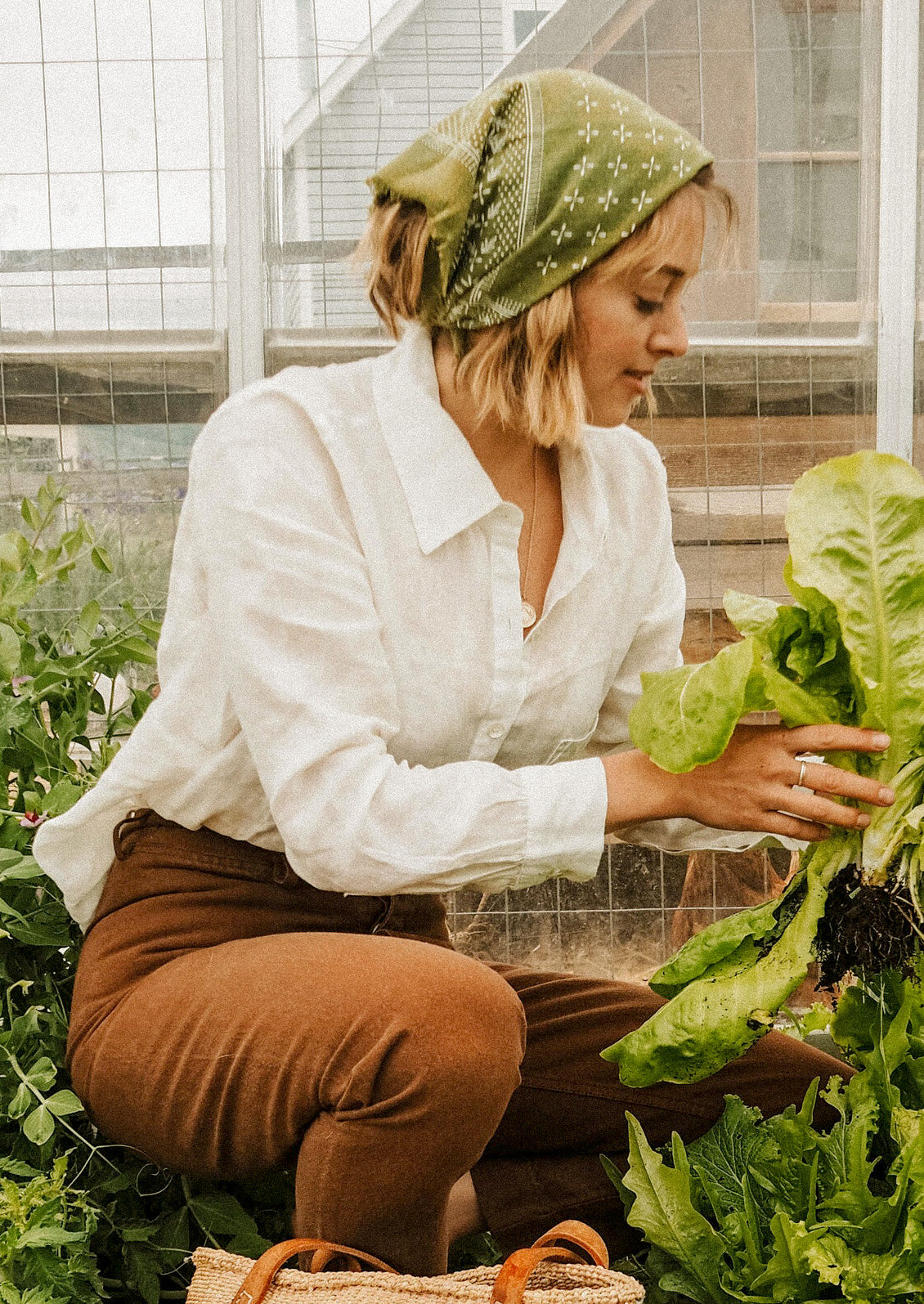 A woman gardening and wearing an olive colored bandana on her head.