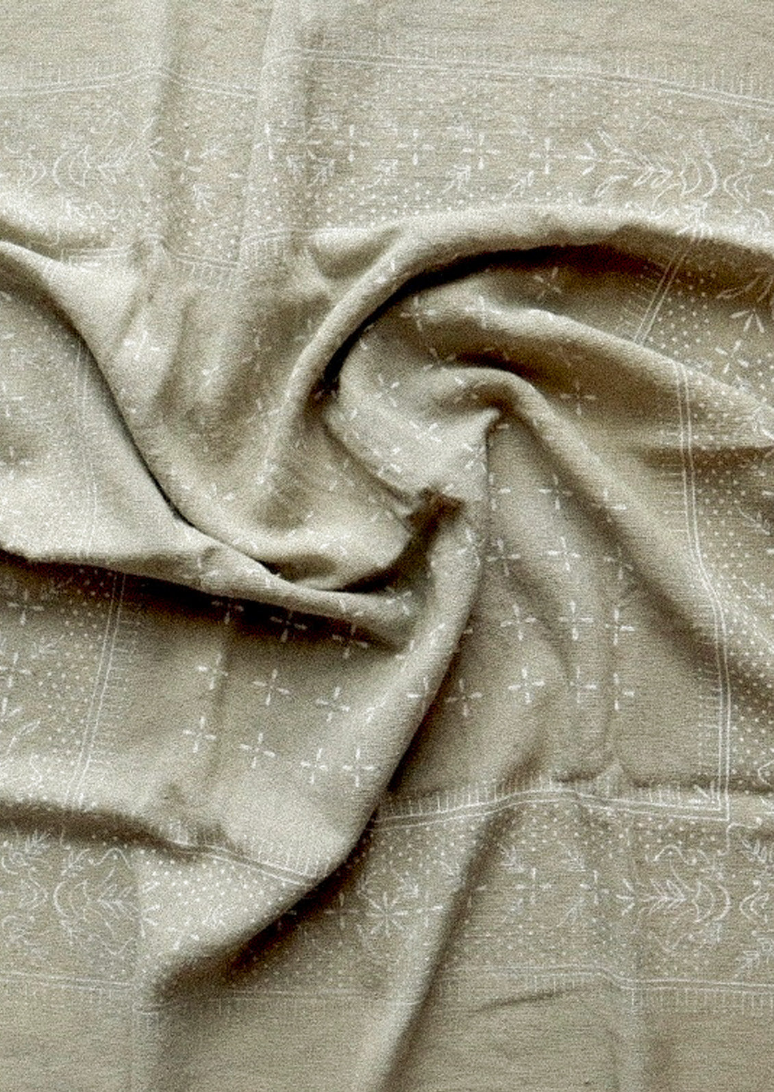 A sage colored patterned scarf that is bunched up in the center.