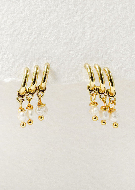 A pair of gold earrings featuring three half hoop and three faux pearls dangling from each earring.