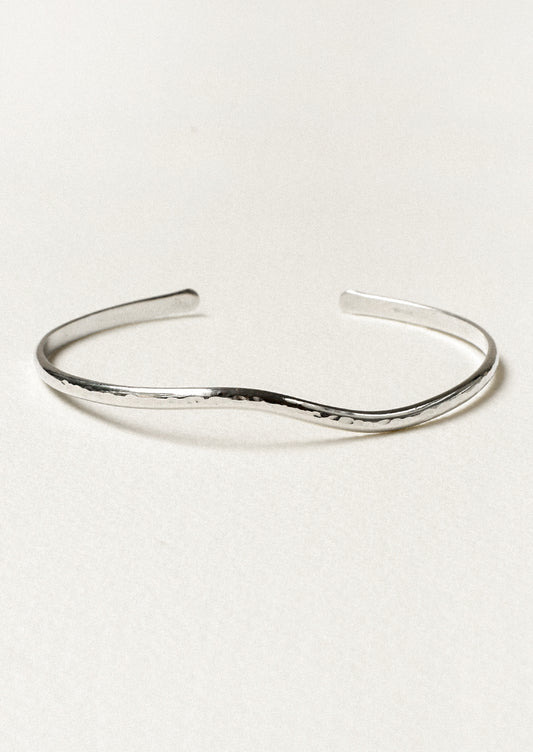 A minimal silver cuff bracelet with a wave-like design.