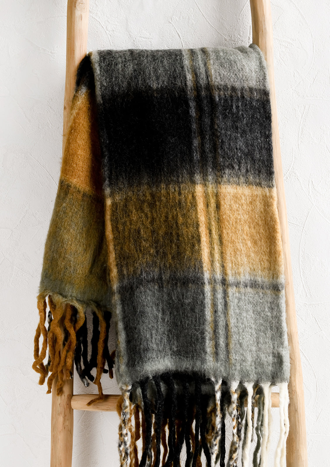 A mohair throw blanket with plaid pattern in grey, black and caramel.