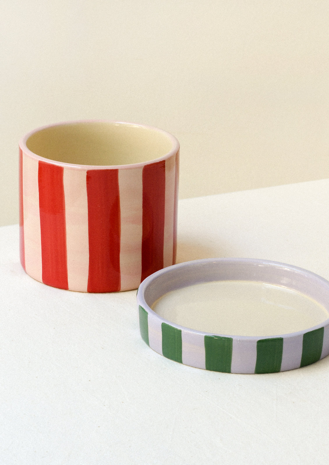 A colorful red and pink striped ceramic planter with a striped green and purple saucer.
