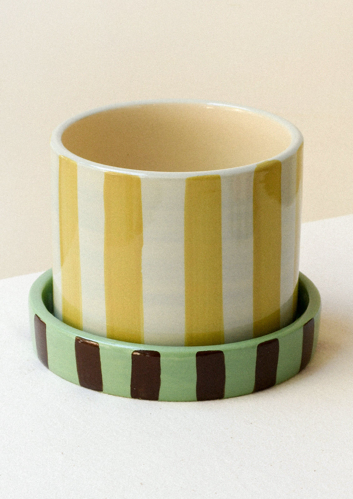 A colorful yellow and white striped ceramic planter with a striped green and brown saucer.