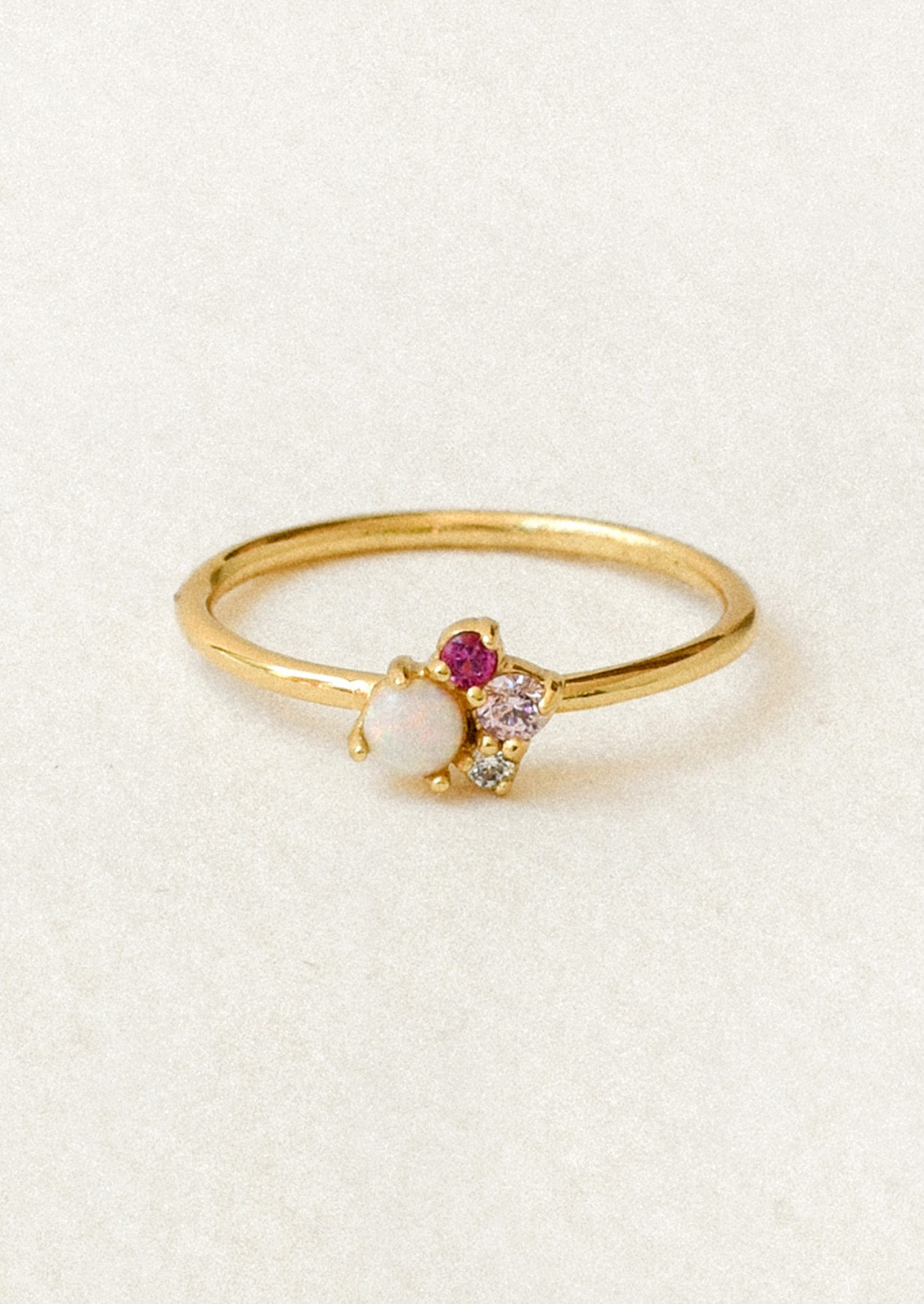 A gold ring with a cluster of gems including a simulated opal and three other small pink and clear gems.