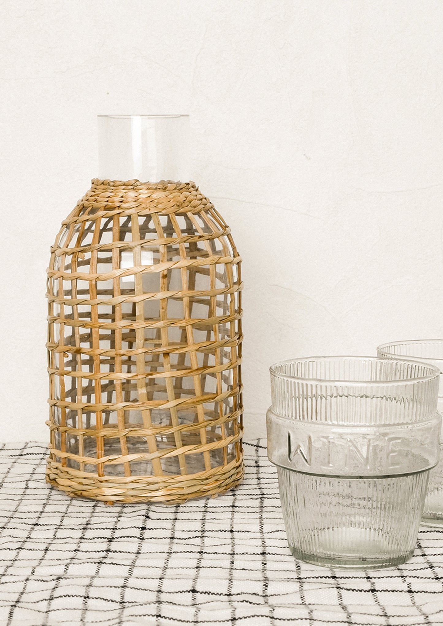 Woven rattan vase and glass container on a checkered surface with a white background