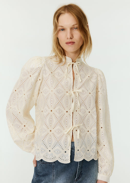 A woman wearing a cream lace blouse with mandarin collar and triple bow tie closure at front.