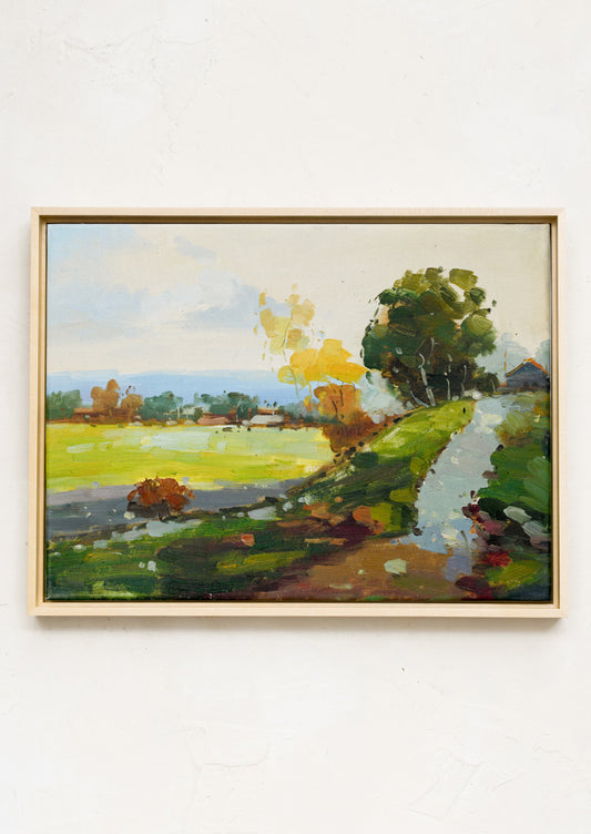 A framed landscape painting in bright yellow, green and blue tones depicting a hillside.