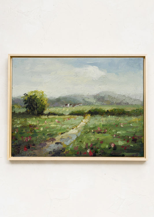 A framed original landscape oil painting of a green meadow with flowers.