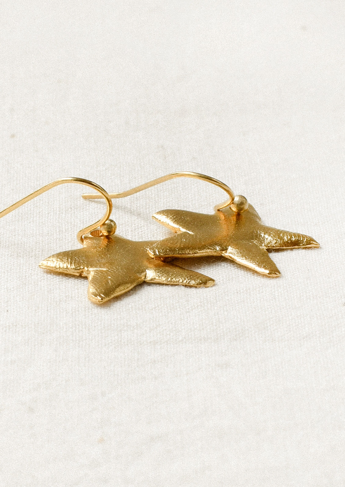 A pair of gold earrings with large dangling star shaped charms.