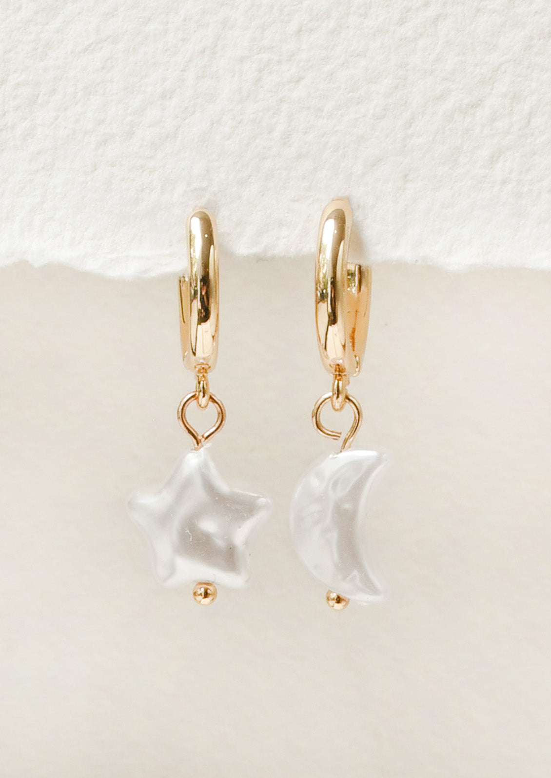 A pair of gold hoop earrings with large star and moon-shaped faux pearl charms.