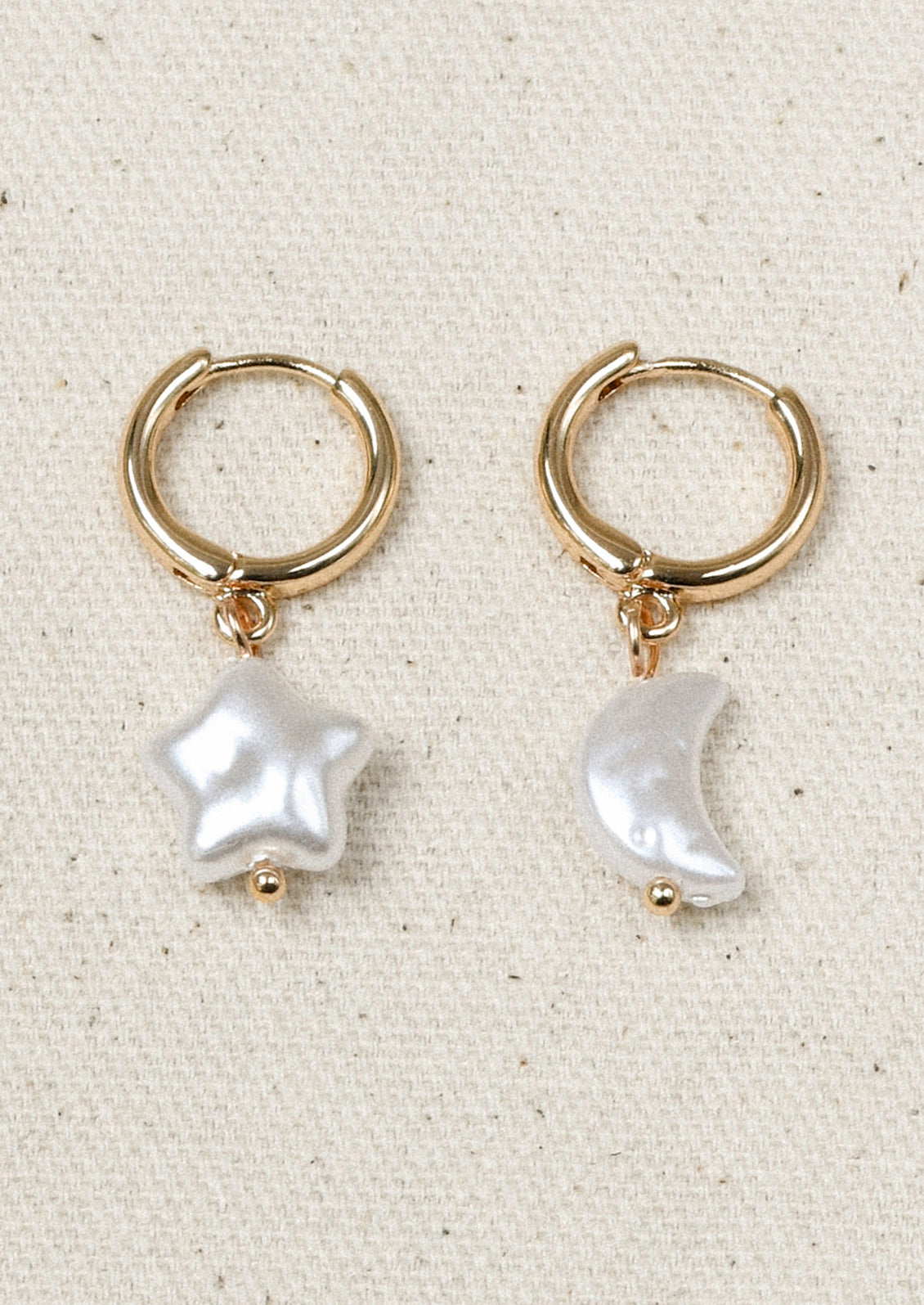 A pair of gold hoop earrings with large star and moon-shaped faux pearl charms.