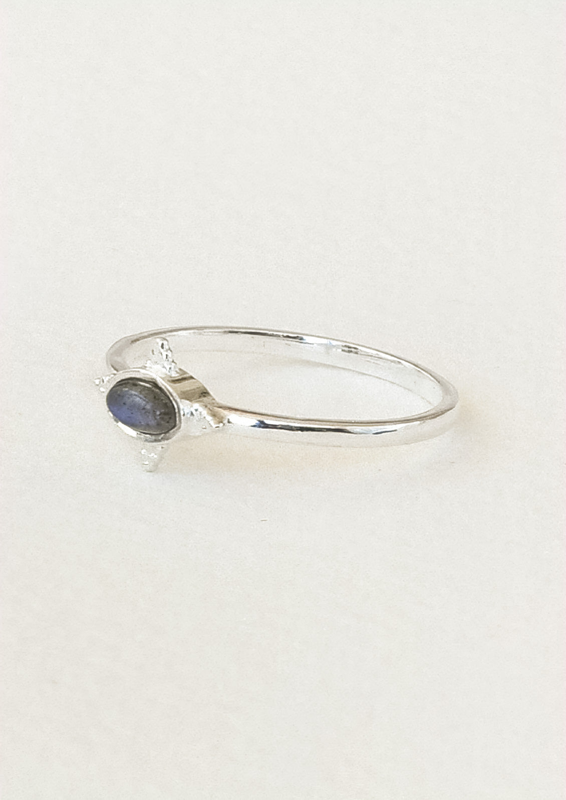 Side view of a sterling silver ring with a dark grey oval labradorite stone framed in a star shaped setting on a white paper.