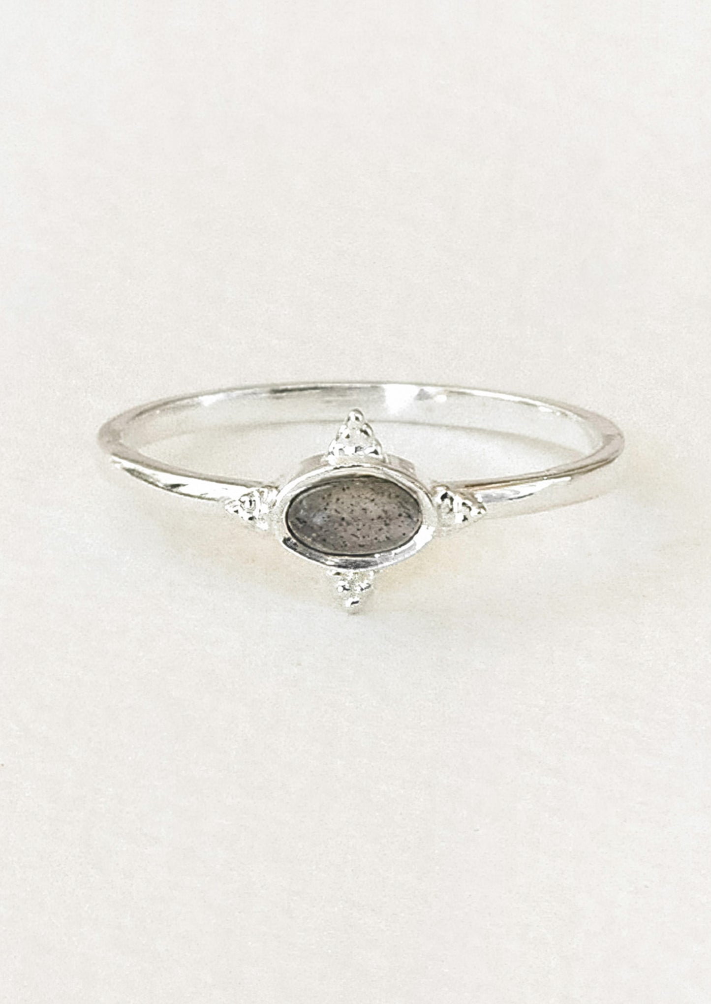 A sterling silver ring with a dark grey oval labradorite stone framed in a star shaped setting on a white paper.