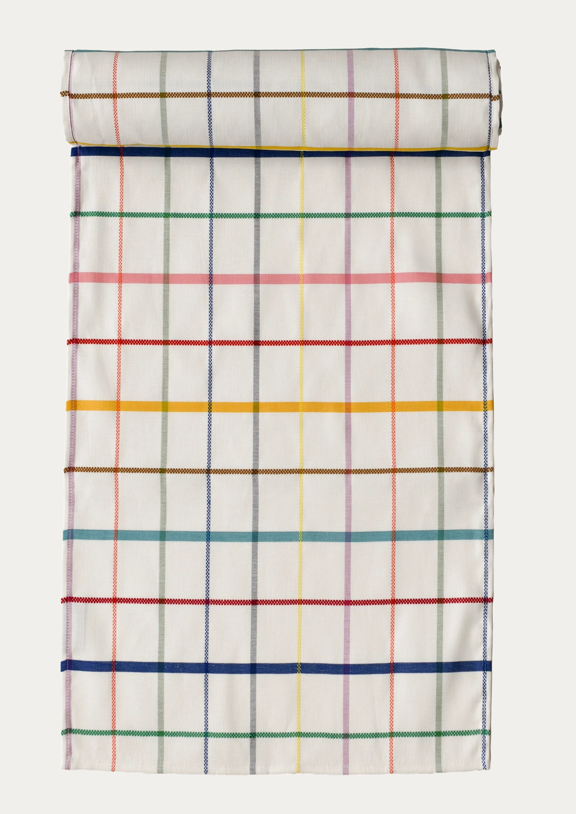 A table runner featuring a multicolor plaid pattern on a white background, shown against a light gray studio backdrop.