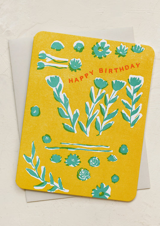 A yellow greeting card with floral print, red lettering reads "Happy Birthday".