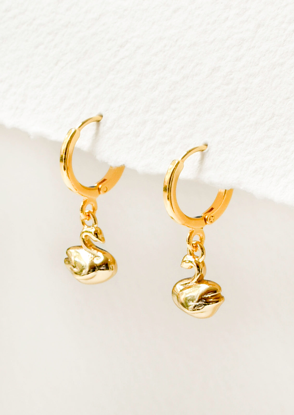 A pair of gold hoop earrings with a gold dangling swan charm.