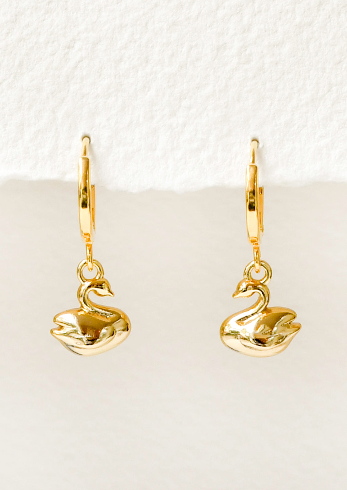 A pair of gold hoop earrings with a gold dangling swan charm.