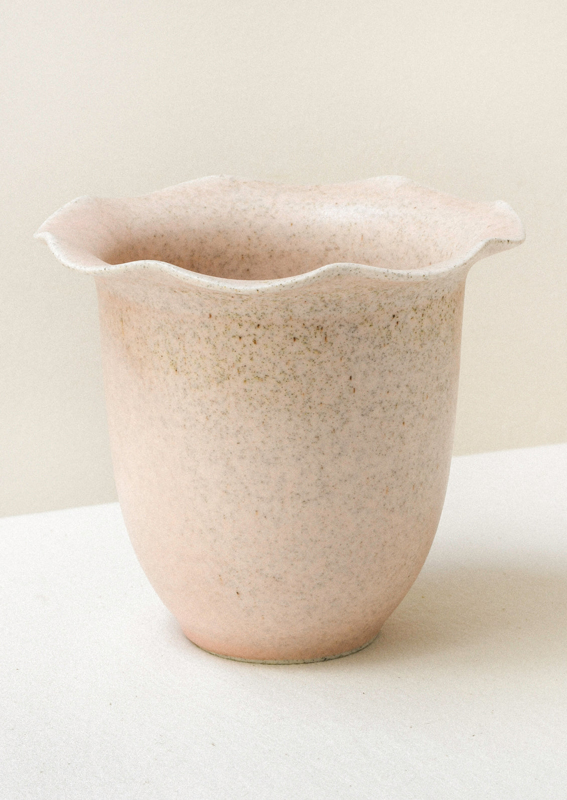 A light pink ceramic speckled vase with a rippled lip design.