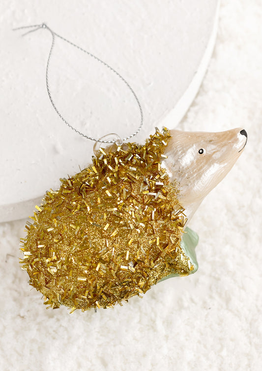 A holiday ornament of a hedgehog in gold tinsel.