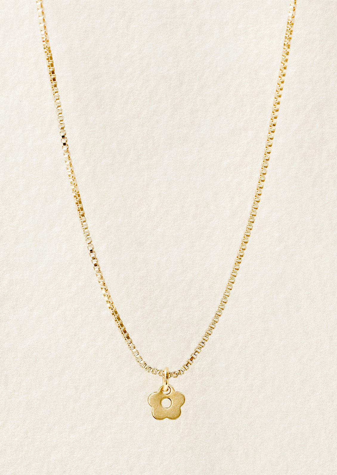 A gold chain necklace with a tiny daisy charm in front of a white background.